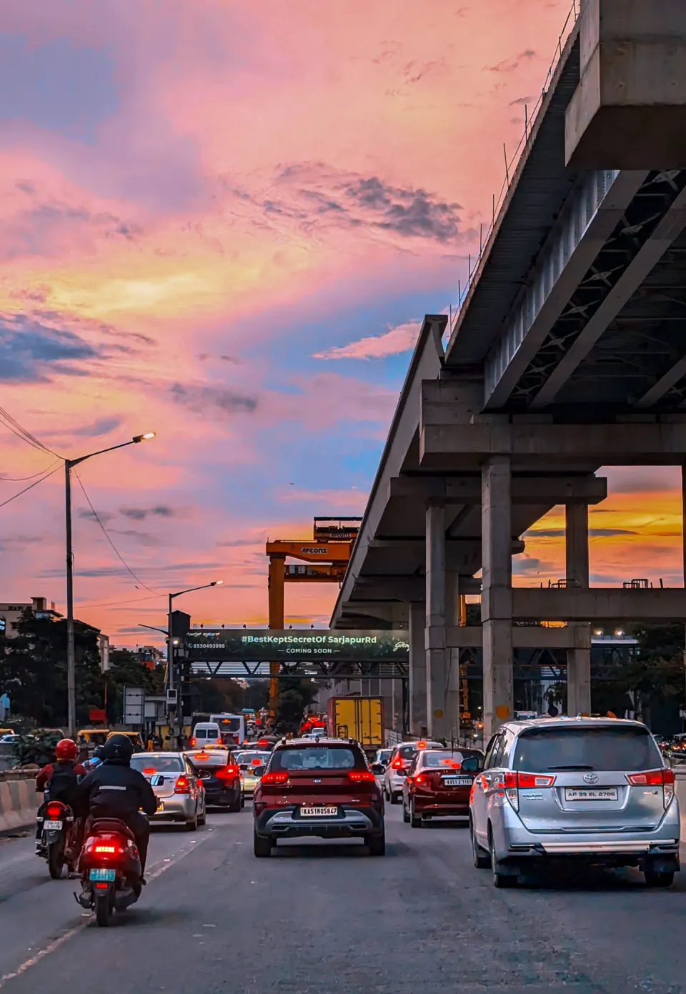 Evening traffic on a multi-lane road in Bengaluru beneath an elevated viaduct under construction