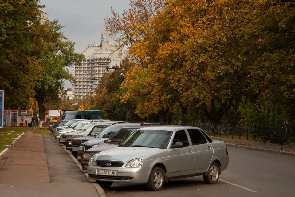 A silver saloon car parked at the kerb on a quiet tree-lined residential street in autumn